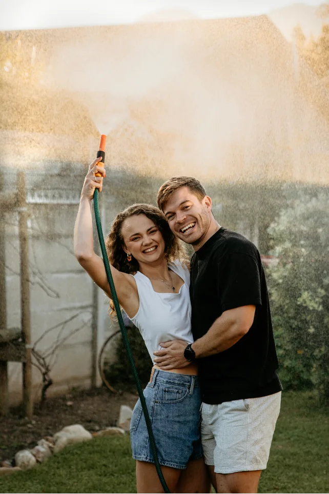 Leane holding a hose up over them while Anru hugs her